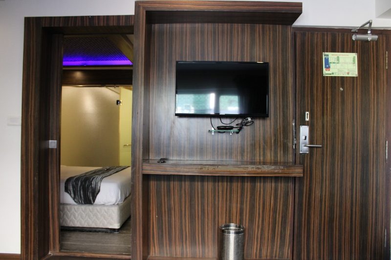 Room entrance with a wood-panelled wall, wall-mounted TV and a view of the bed